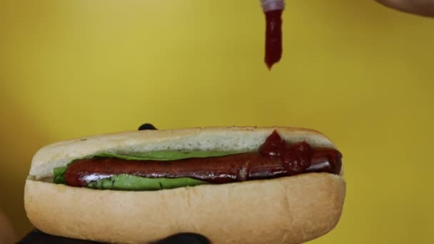黄色い背景にソーセージとマスタードを入れたホットドッグを入れるケチャップ — ストック動画