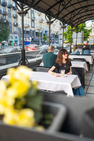 stock image beautiful brunette woman wear jeans suit and sunglasess sits in an outdoor cafe and looking at the camera.