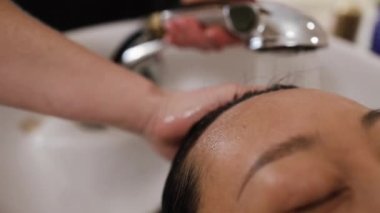 Asyalı genç bir kadın kuaförde uzanmış, yatağını yıkıyor, saçını profesyonel stilist yıkıyor. Kuaför kuaförde ya da kuaförde masaj yaparken kendini rahat ve mutlu hisseden güzel bir müşteri.