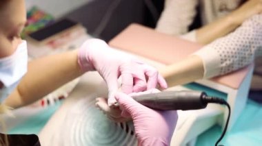 Manikür ve pedikür ustası tırnak cilasını temizler. Yakın plan manikür. Tırnak uzantıları. Manikürcü, değirmen kesicisiyle çalışıyor. Çizgi ışıklarındaki çiviler. Malzeme kaldırılıyor