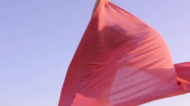 Şehvetli Asyalı kız gökyüzünde rüzgarla dans eden kırmızı kanat çırpan bez sallıyor ve arka planda güneş parıldıyor. Şefkat kavramı.
