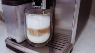 Close-up of a transparent glass with hot and delicious drink with milk and vanilla poured from the coffee machine.