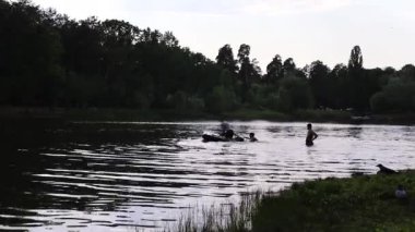 Arkadaşların yaz gölünde gece su sıçratıyor. Yüzen ve suda eğlenen gençlerin silueti. Dikkatsizlik ve mutlu bir çocukluk. Yaz tatili. Kırsal kesimde açık hava aktiviteleri