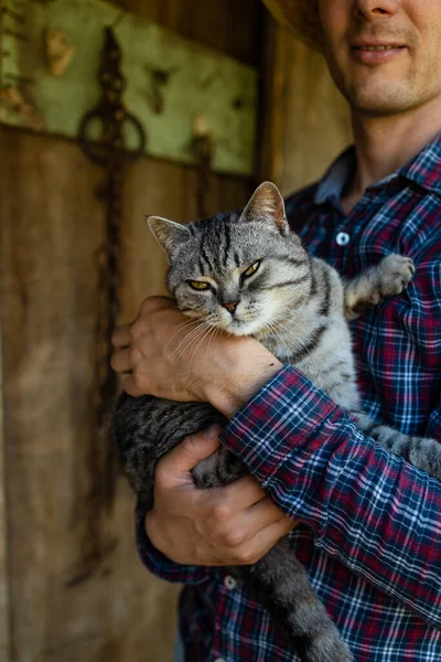 村の屋外で小さな子猫を手に幸せな若いひげを生やした農家 変な可愛いペットと遊ぶわら帽子の笑顔の男 田舎でお楽しみください — ストック写真