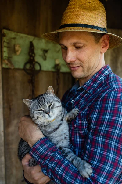 村の屋外で小さな子猫を手に幸せな若いひげを生やした農家 変な可愛いペットと遊ぶわら帽子の笑顔の男 田舎でお楽しみください — ストック写真