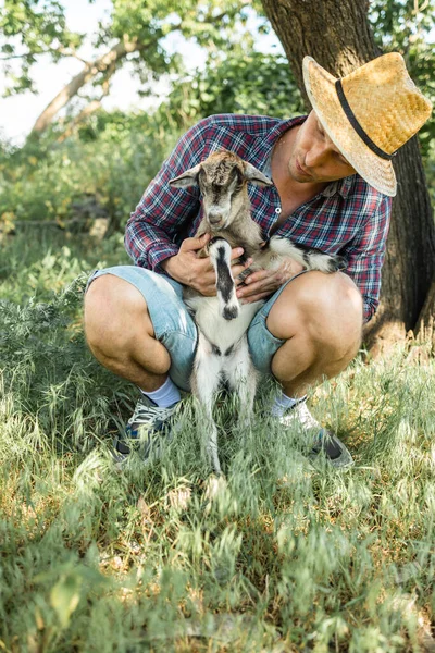 a man of Caucasian appearance, a farmer holds and hugs his favorite goat. a small goat. The concept of a summer countryside. Close to outdoor recreation.