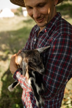 Kafkas görünümlü mutlu bir adam, bir çiftçi en sevdiği keçisini kucaklar ve kucaklar. Küçük bir keçi. Yazın kırsal alan kavramı. Açık hava eğlencesine yakın.