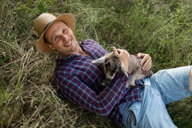 Kafkas görünümlü mutlu bir adam, bir çiftçi en sevdiği keçisini kucaklar ve kucaklar. Küçük bir keçi. Yazın kırsal alan kavramı. Açık hava eğlencesine yakın.