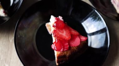 Masadaki siyah tabakta çilekli cheesecake..