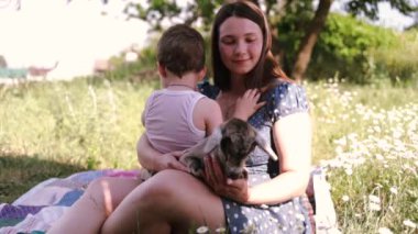 Hayvanlarla otlakta bir aile. Anne ve bebek kırsal bölgedeki yeşil bir çayırda küçük bir keçiye dokunuyor.