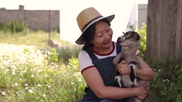 年轻的亚洲女人抱着可爱的小山羊坐在绿地里 — 图库视频影像