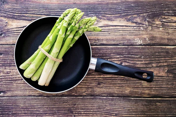 stock image Asparagus cooking concept, top down view on frying pan with fresh bunch of asparagus, lying down on a kitchen table, spring healthy cooking idea