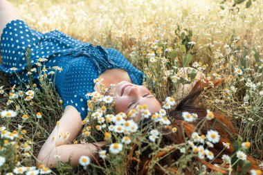 Sarışın güzel bir kadının papatya tarlasında yatarken fotoğrafı, papatya çayır kokusunun tadını çıkaran tatlı bir kadın, çiçek tarlasında rahatlamış, bahar doğasında eğlenen tatlı bir genç kız..