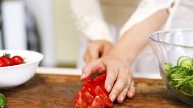Kesme tahtasındaki taze domatesleri kesmek için bıçak kullanan bir kadın. Yakın plan. Evde vişneli domates kesen bir kadın. Ev yemeği hazırlıyorum..