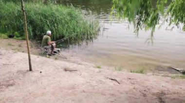 Yaşlı balıkçının gölün kenarında oturup balık tutuşu. Kafkasyalı bir adam sakin ve rahat vakit geçiriyor..