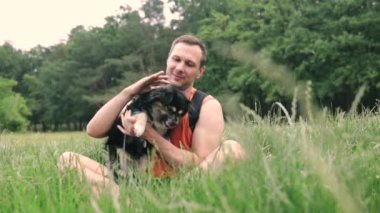 Şirin küçük köpek ve sahibi parkta birlikte oynuyorlar. Kürklü köpek okşamayı ve insanın en iyi arkadaşıyla iyi vakit geçirmeyi sever. Parktaki çimlerde eğleniyorum. Koşumlu köpek.