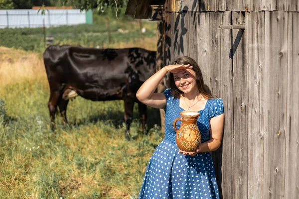 Young farmer woman smiling on camera carries jug of milk after milking cow on farm pasture. Natural dairy products from farmer for healthy diet .Breeding cattle on village field. Natural food.