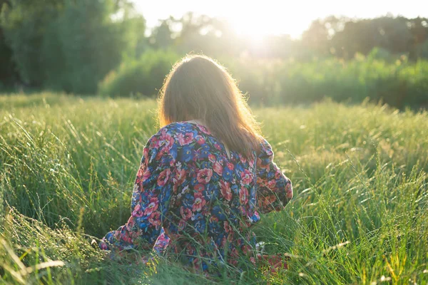 stock image A woman relaxing in nature on the green grass in the park at sunset.