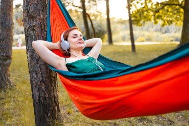 Genç bir kadın sonbahar ormanında hamakta müzik dinliyor..