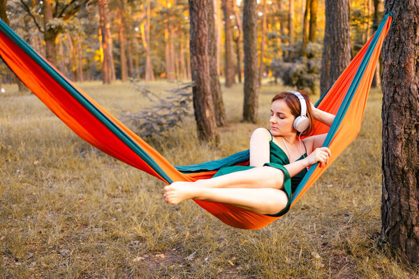 Young woman listening to music in hammock in the autumn forest.