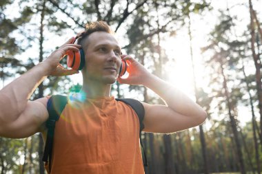 Spor takımındaki genç adam sırt çantası ve kablosuz kulaklıkla hafta sonları ormanda yürürken müzik dinliyor.