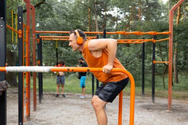 Fitness, spor, eğitim ve yaşam tarzı kavramı - müzik dinleme ve yatay çubuk açık havada egzersiz kulaklık ile genç adam