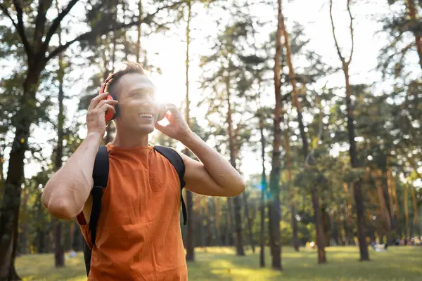 stock image Young man in sports wear with backpack and wireless headphones listening to music while walking in woodland in weekend