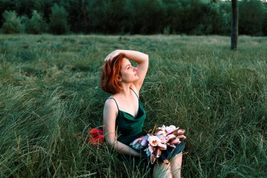 Elinde nilüfer çiçekleri tutan güzel bir genç kadının yaz portresi. Çim tarlasında otururken. Güneşin tadını çıkarıyorum. Mutluluk ve aşk kavramı. Kaybolan gözler.