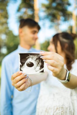 Happy pregnant couple sitting on the grass in park. Happy and young pregnant couple hugging in nature.