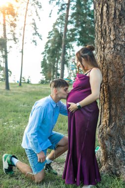 Genç hamile bir çift yaz günü büyük bir ağaca yaslanıyor. Genç hamile çift dışarıda biraz vakit geçiriyor..