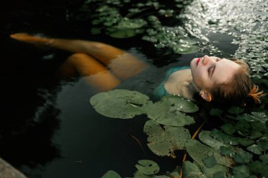 Mavi elbiseli güzel sarışın bir kız su zambaklarıyla nehirde poz veriyor. Ophelia 'nın peri masalı. 