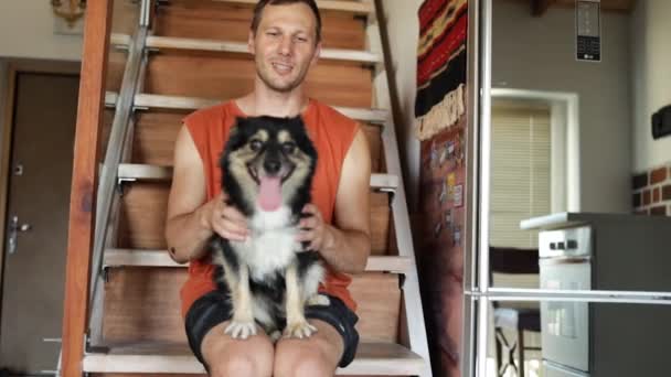 自宅で彼の腕の中で彼の犬と階段に座っている男 — ストック動画
