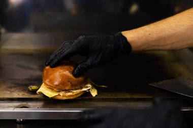 Siyah eldivenli şef hamburger pişiriyor. Yatay fotoğraf. Siyah arka planda tanınmayan bir fotoğraf. Boşluğun kopyası.