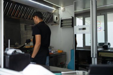 Siyah üniformalı şef küçük kafede hamburger pişiriyor..