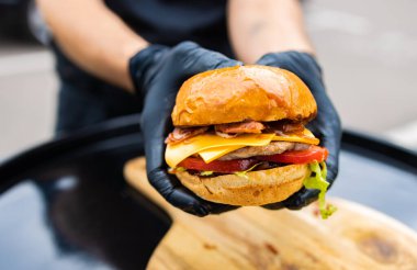 Siyah eldivenli şef hamburger pişiriyor. Yatay fotoğraf. Siyah arka planda tanınmayan bir fotoğraf. Boşluğun kopyası.
