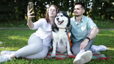 Şirin köpekli genç çift yaz parkında yeşil çimlerde selfie çekiyor..