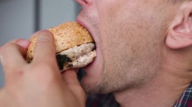 Tıraşsız, beyaz bir adam zevkle et burger yer, ağzıyla burger yer, abur cubur yer, evde ketçap sosu sürer..