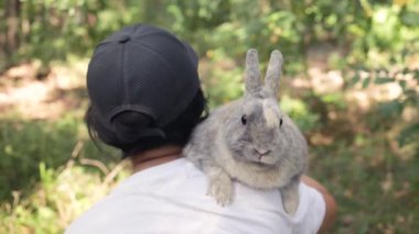 Tavşanlı bir adamın yakın portresi. Gri tüylü bir tavşan ormanda sahibinin omzunda oturuyor. Hayvanla seyahat et..