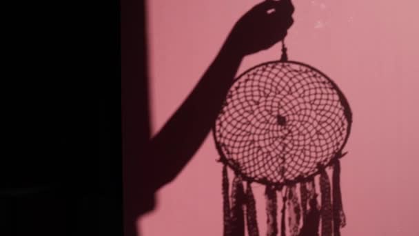 ピンクの壁のドリームキャッチャーの影 ピンクの背景に女性の手のシルエットのドリームキャッチャー — ストック動画