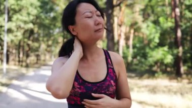 Genç Asyalı fitness kadını spor sakatlığını boynunda tutuyor, antrenman sırasında kas ağrısı çekiyor.
