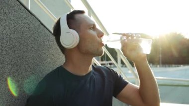 Kapalı yerde genç adam parkta koştuktan sonra şişeden su içer. Sağlıklı insanlar, yaşam tarzı eğitimi, formda erkek sporcu, ağır çekimde koşuyor.
