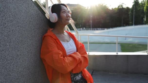 Krásná Asijská Žena Oranžové Kombinéze Sluchátka Poslech Hudby Ulici — Stock video