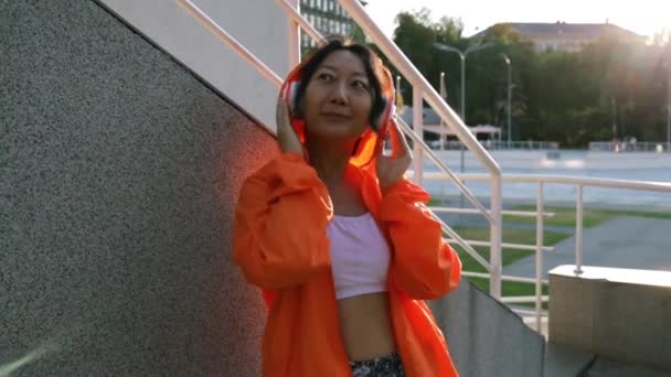 Vacker Asiatisk Kvinna Orange Overall Och Hörlurar Lyssnar Musik Gatan — Stockvideo