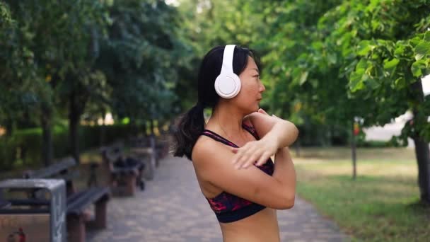 Azji Średnim Wieku Kobieta Odzieży Sportowej Słuchawki Rozciągające Ramiona Parku — Wideo stockowe