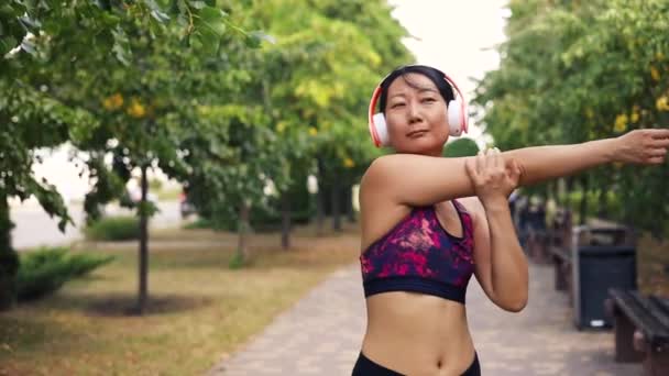 Azji Średnim Wieku Kobieta Odzieży Sportowej Słuchawki Rozciągające Ramiona Parku — Wideo stockowe