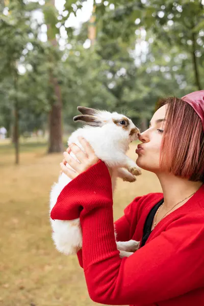A young woman in a red sweater kisses a white rabbit in the park