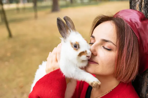 赤いセーターの若い女性が公園で白いウサギにキス — ストック写真