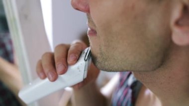 Bir adam evde banyoda aynanın karşısında dikilirken bıyık ve sakal kesmek için elektrikli tıraş makinesi kullanıyor..