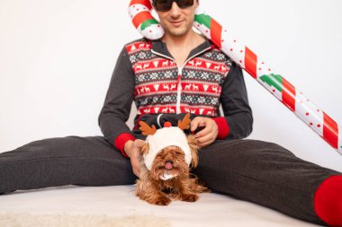 Beyaz arka planda köpeği olan Noel Baba şapkalı komik bir genç adam..