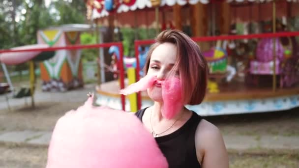 夏の遊園地で大きなピンクの綿菓子を楽しんでいる幸せな女性のクローズアップポートレート — ストック動画